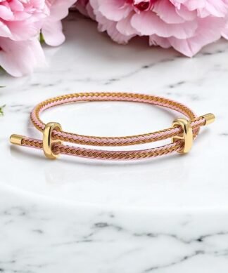 Bracelet tressé rose clair et doré pour femme avec fermoir doré, bijou minimaliste sur marbre blanc décoré de fleurs roses.