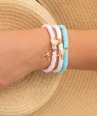 Bracelets fantaisie pastel femme style été avec charms dorés étoile de mer et coquillage, posés sur robe en crochet blanc